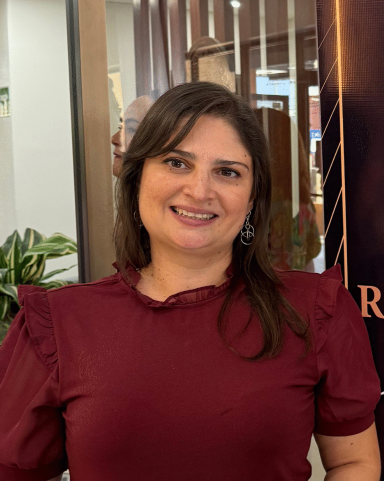 La imagen muestra a Verónica Portillo Reyes sonriendo, vistiendo una blusa color vino, con el cabello suelto, posando frente a un fondo interior con plantas y paneles decorativos.